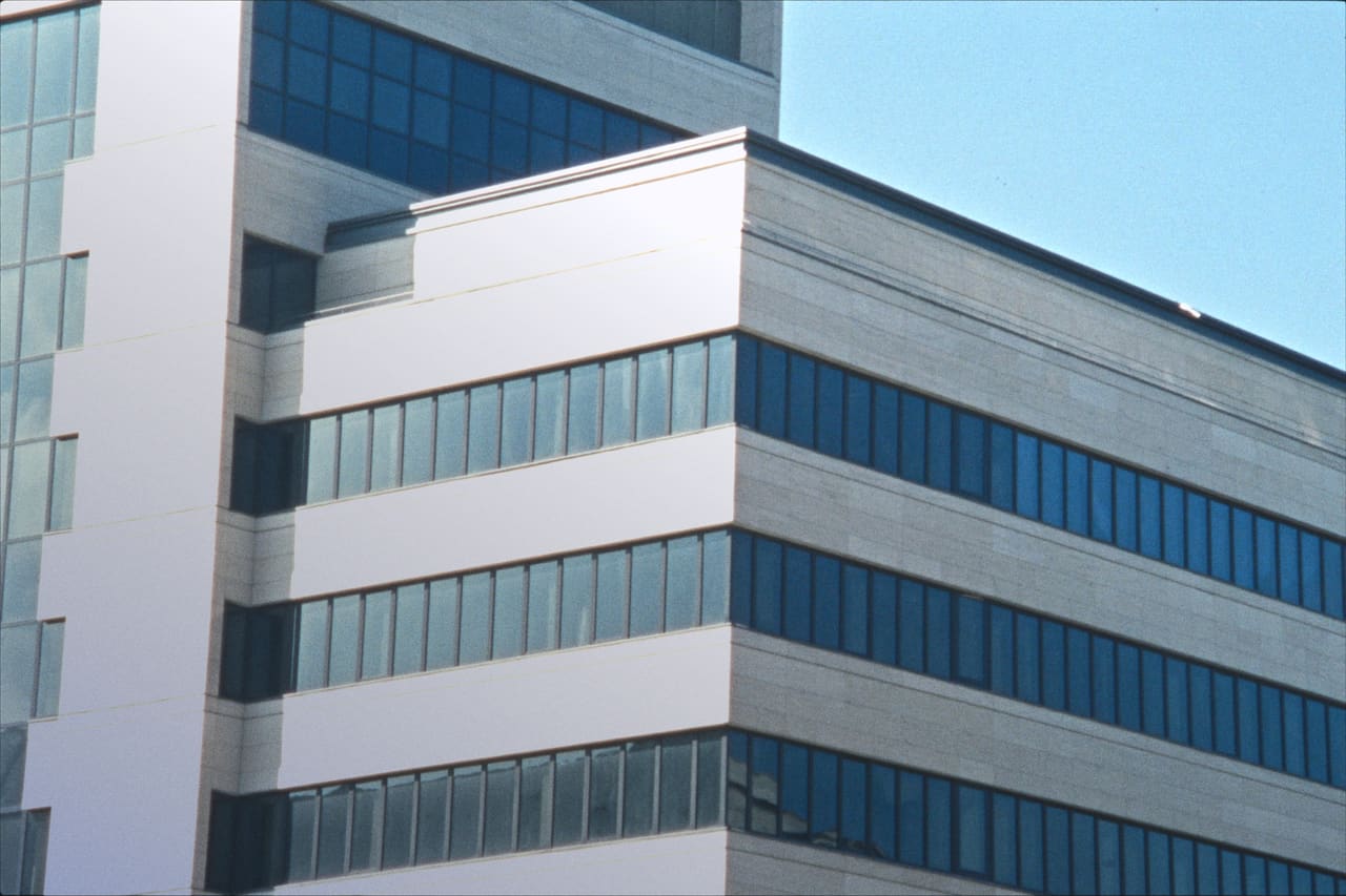 Esquina de un edificio de oficinas contemporáneo: bandas de piedra clara y vidrio azulado contra el cielo.